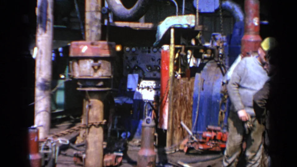 1970 United Kingdom 8mm frame showing machinery, pipes, tools, and a partially visible worker in a yellow hard hat.
