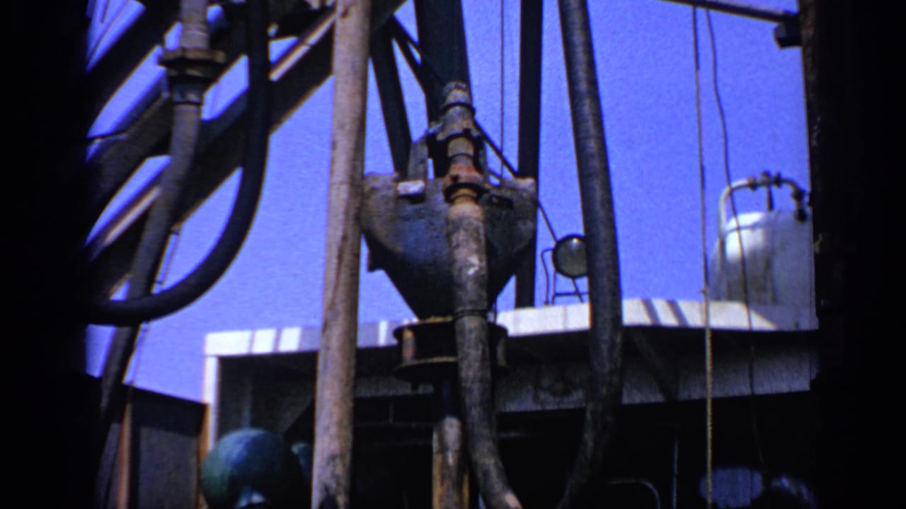 Close view of oil-rig pipes and hoses against a bright blue sky.