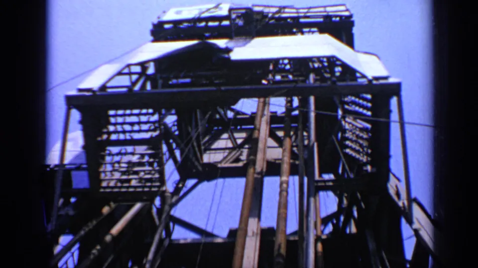Wider 1970 UK oil-rig frame showing a derrick structure, platforms, ladders, rigging, and vertical supports.