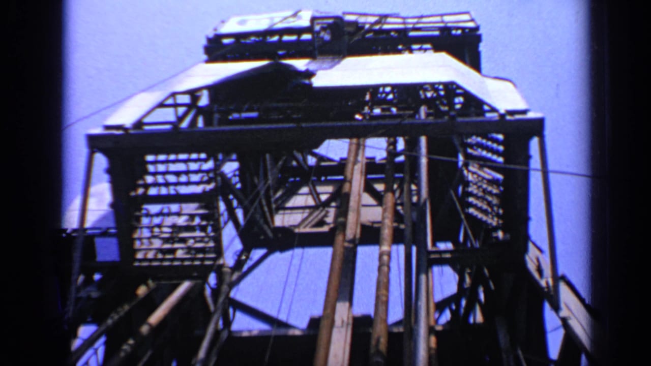 Low-angle view of a metal oil rig structure against blue sky.