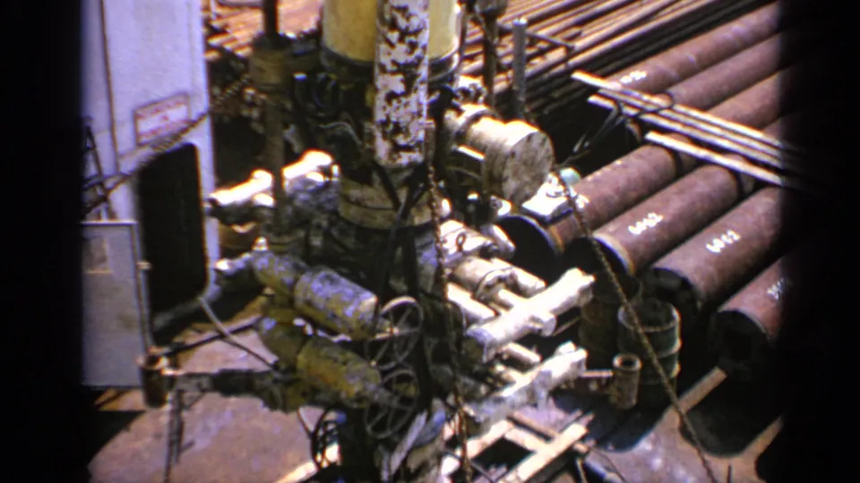 Close 1970 United Kingdom view of oil-rig pipework, valves, cables and stacked cylindrical pipe sections on 8mm film.