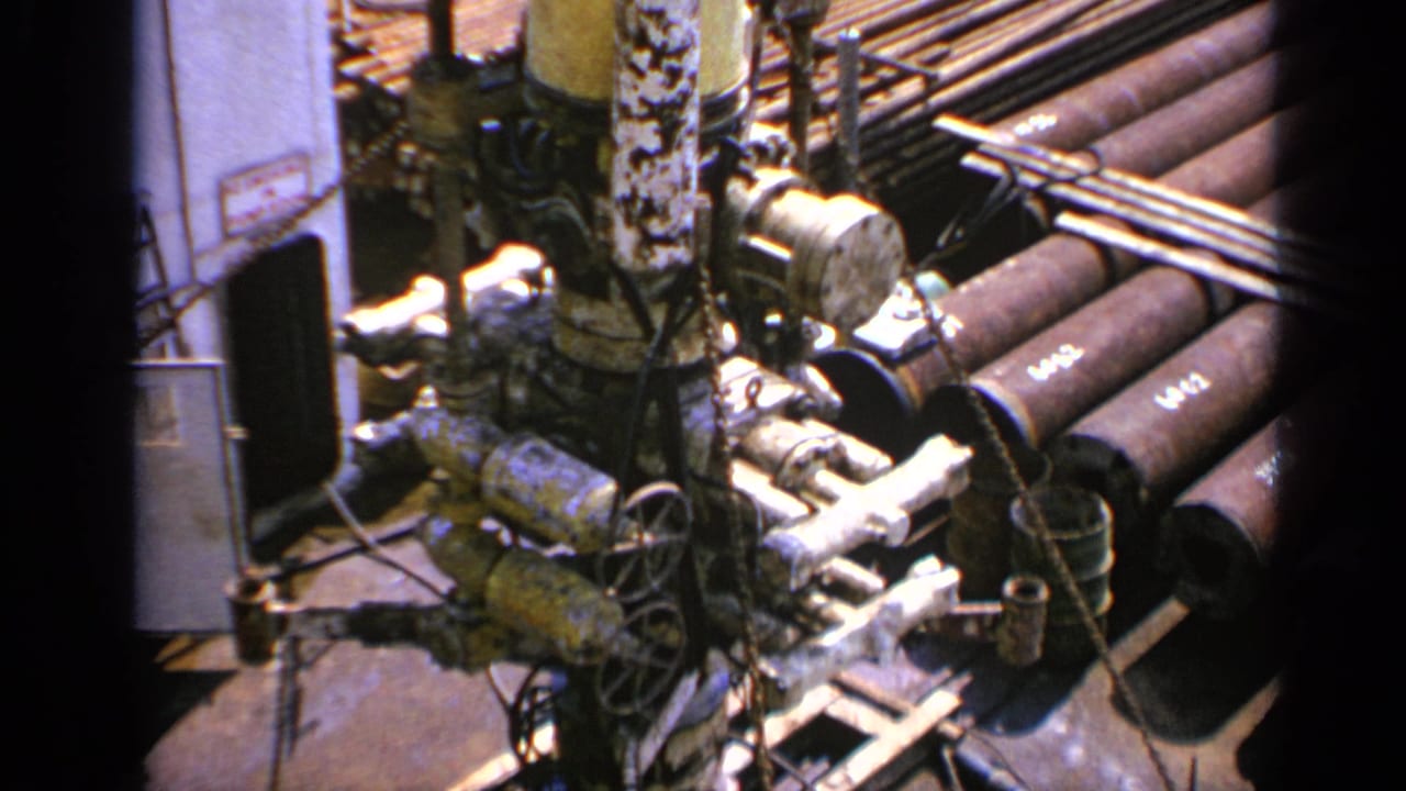 1970 United Kingdom 8mm frame showing weathered industrial machinery, valves, hoses, and stacked metal pipes from above.