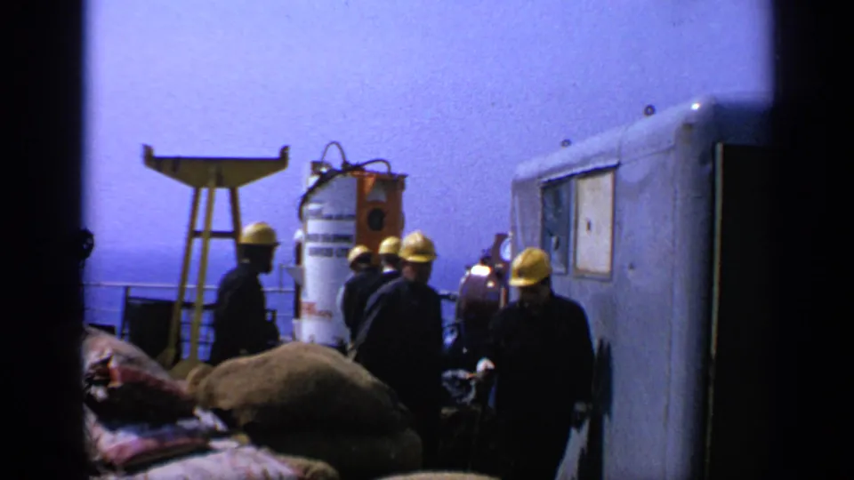 Several hard-hatted workers gather near platform equipment and a cabin-like structure on a 1970 United Kingdom offshore rig.