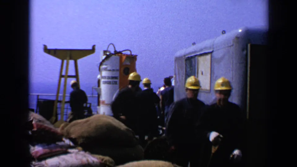 1970 United Kingdom 8mm frame with workers in yellow hard hats near a trailer and a labeled North Sea Diving Services tank.