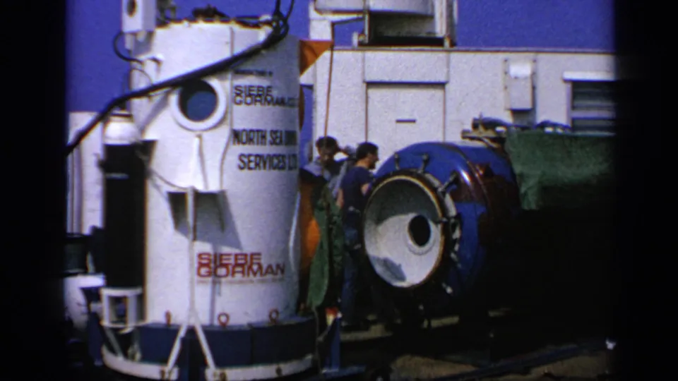 White Siebe Gorman and North Sea Oil Services Ltd cylinder beside workers and a blue module on a maritime platform.