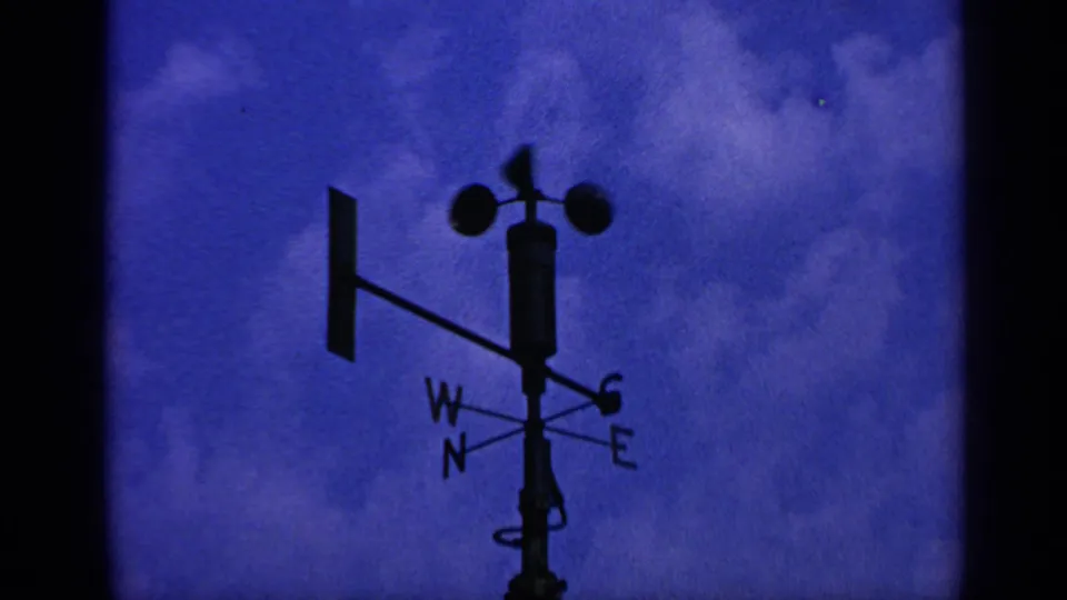 1970 United Kingdom 8mm frame with a dark weather instrument silhouette, compass letters, and blue clouded sky.