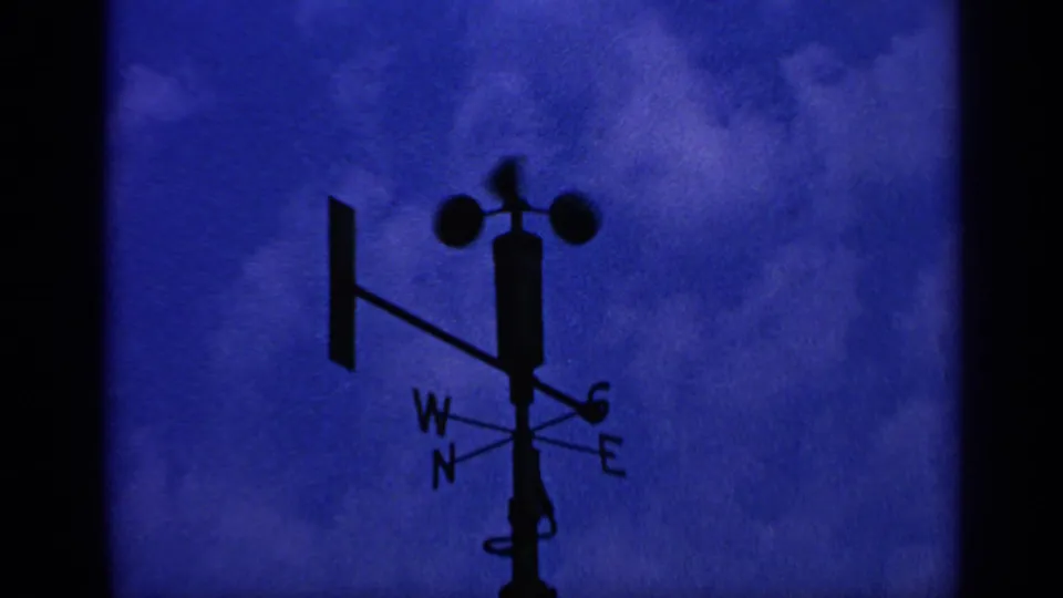 1970 United Kingdom 8mm frame of a silhouetted wind vane and anemometer near the lower frame against blue clouded sky.