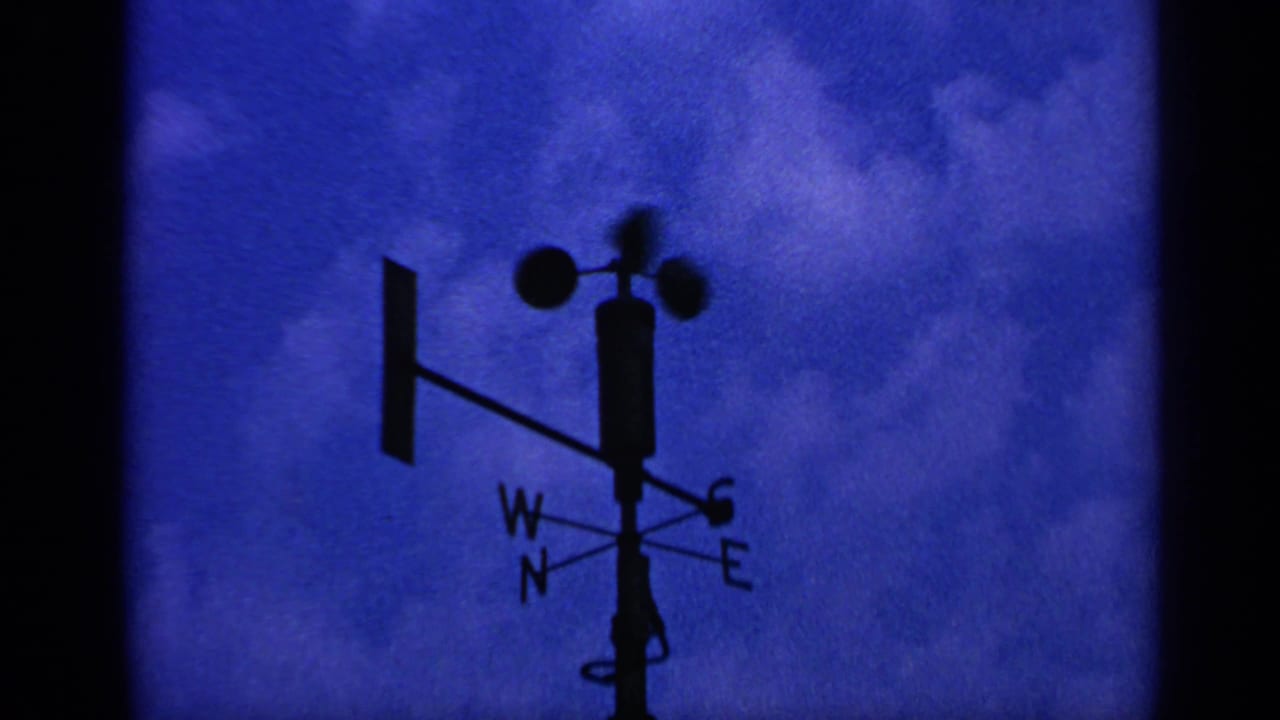 Silhouetted weather vane and anemometer against a deep blue cloudy sky.