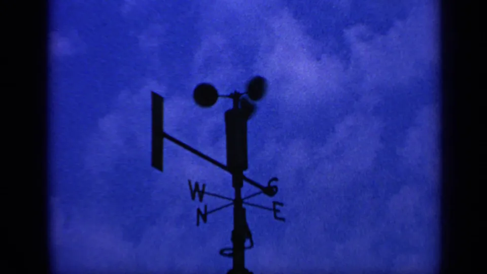 1970 8mm frame with the weather vane and anemometer slightly shifted in silhouette, with W, N, S, and E letters visible.