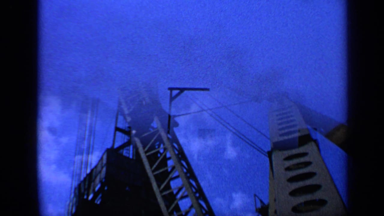 1970 United Kingdom 8mm frame showing a crane structure and cables silhouetted against a deep blue sky with clouds.