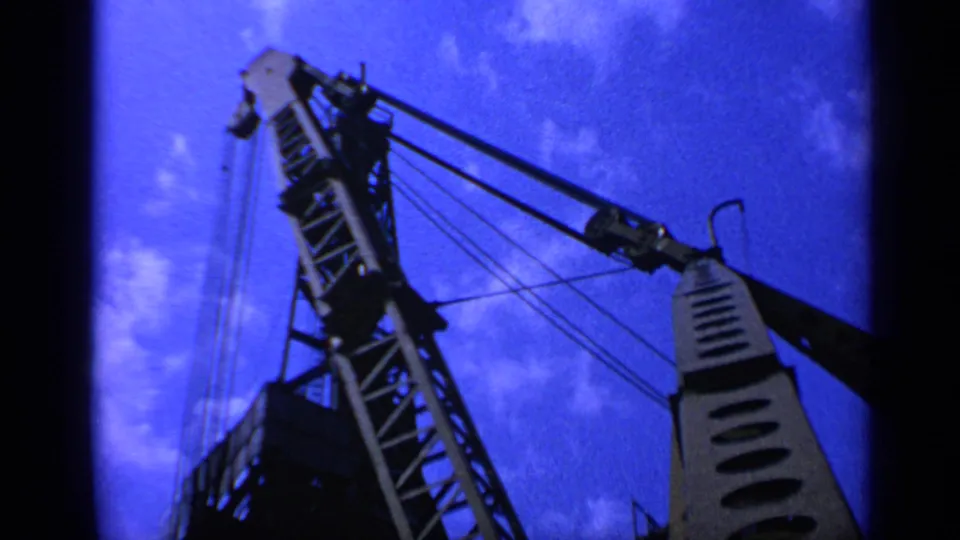 1970 United Kingdom 8mm view of a tall crane mast and boom photographed from below, with cables visible against the sky.