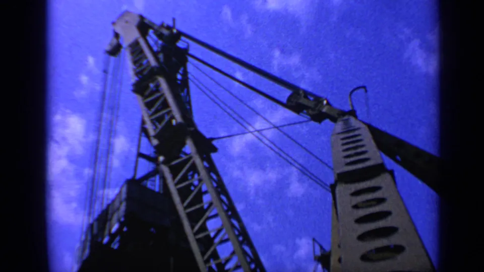 1970s United Kingdom 8mm frame showing the upper crane structure, diagonal boom, and suspended metal fixture from below.