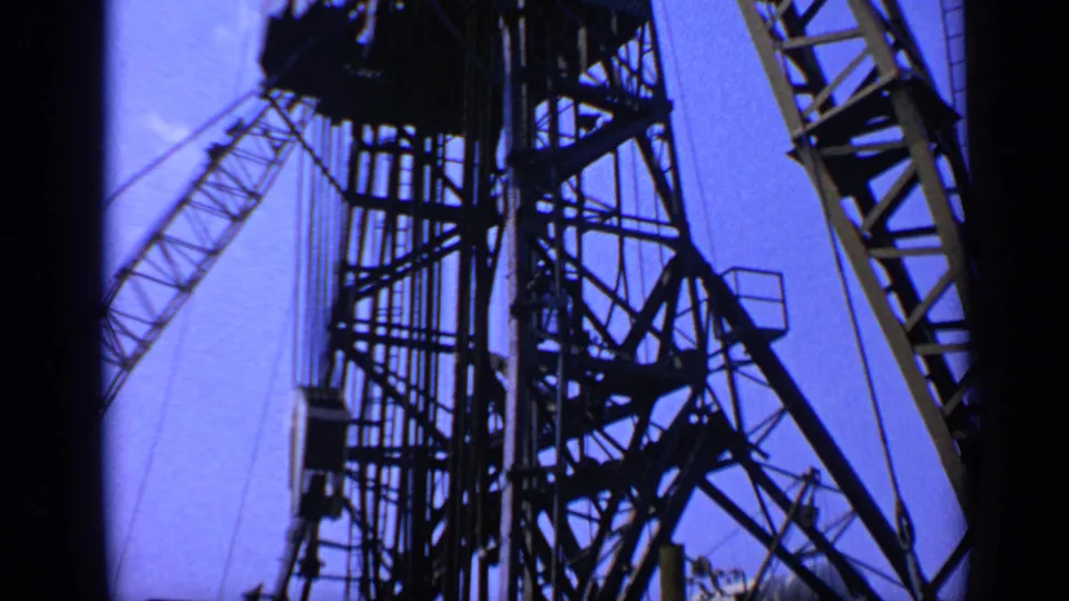 1970s United Kingdom 8mm frame of a tall industrial crane structure, with lattice sections, cables, and a raised boom overhead.