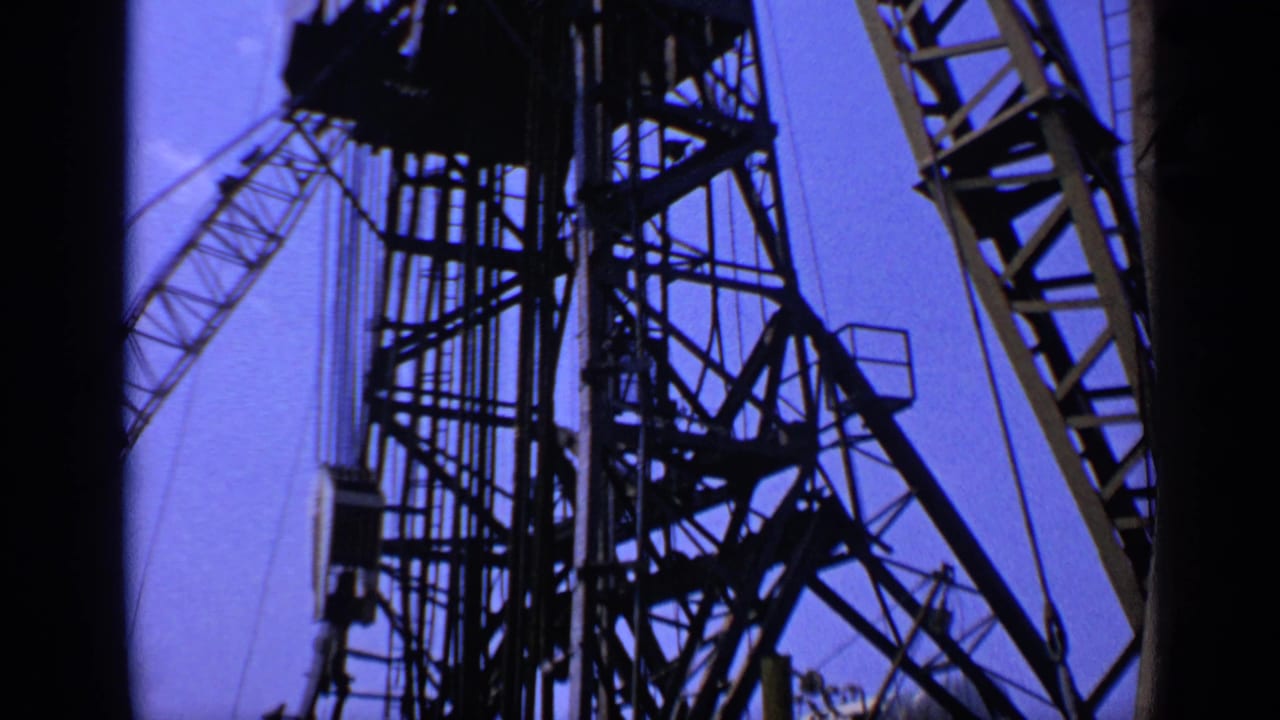 Silhouetted offshore platform framework and crane shapes against a blue sky.
