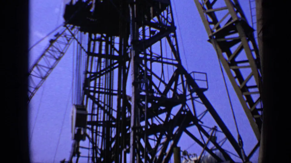 1970 United Kingdom 8mm view of offshore platform steelwork, with diagonal crane framing silhouetted in blue light.