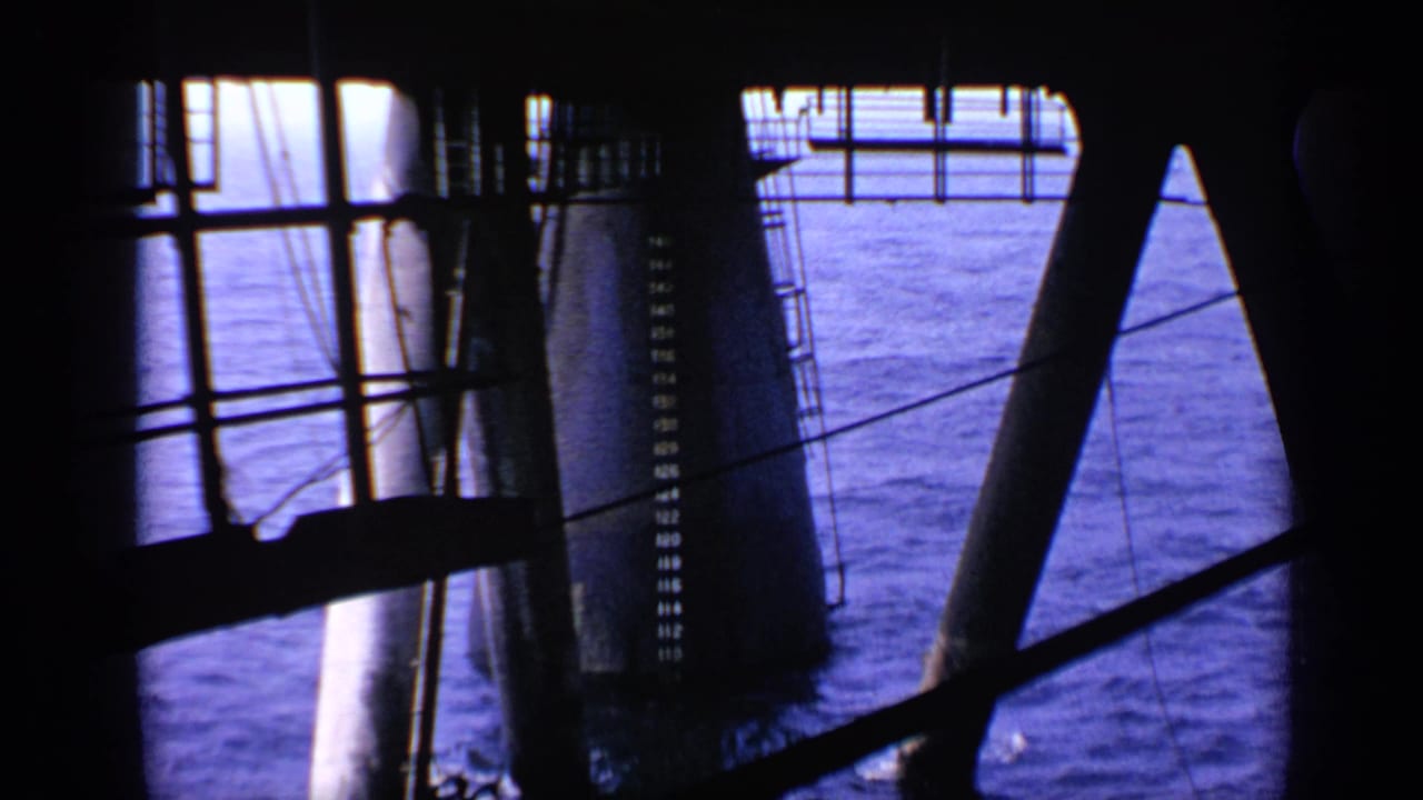 1970 United Kingdom 8mm frame showing heavy offshore structure with pillars, ladders, wires, and open blue water beyond.