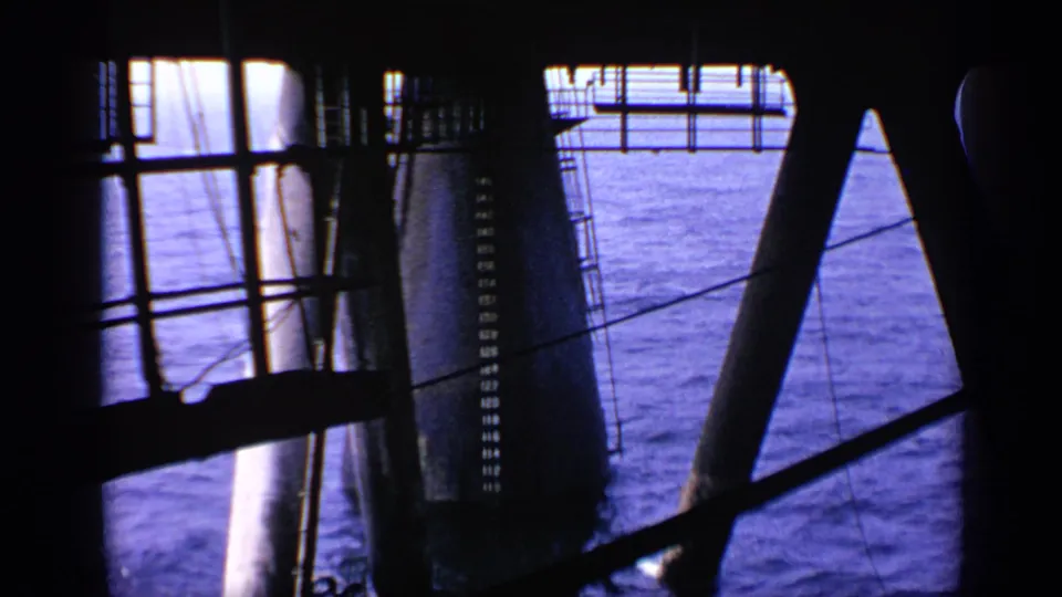 1970 United Kingdom frame with dark beams, a vertical ladder, heavy support pillars, wires, and sea visible through the structure.