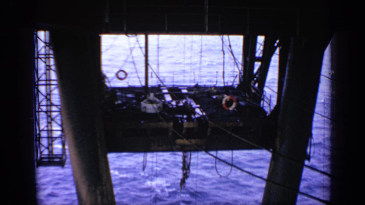 Oil rig platform framed by dark supports above blue open water.