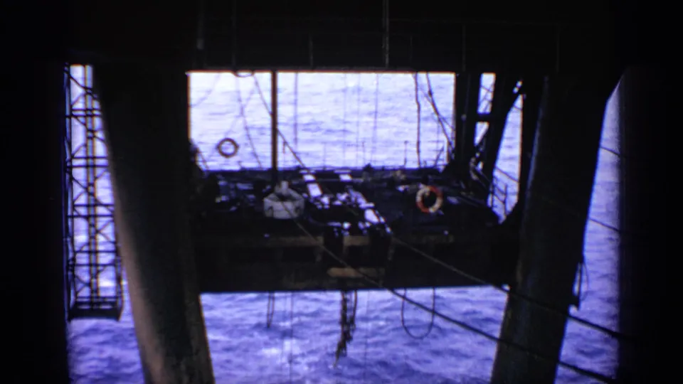 Low-angle 1970 United Kingdom rig view showing a platform, life ring and blue sea beyond the industrial frame.