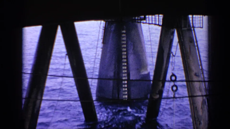 1970 United Kingdom 8mm frame showing water seen through dark structural supports near a large cylindrical pylon.