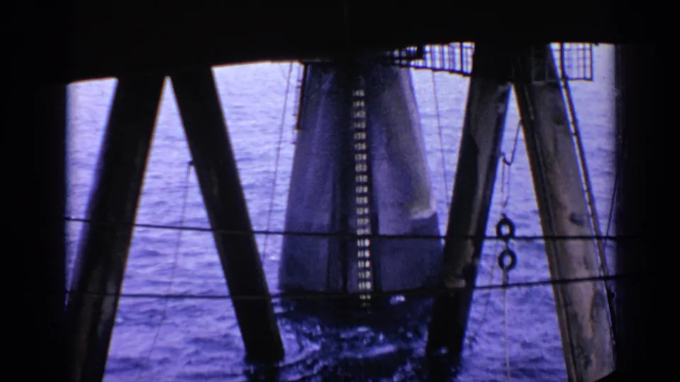 1970 United Kingdom home-movie view of water and heavy coastal structure supports, with a cylindrical pylon at right.