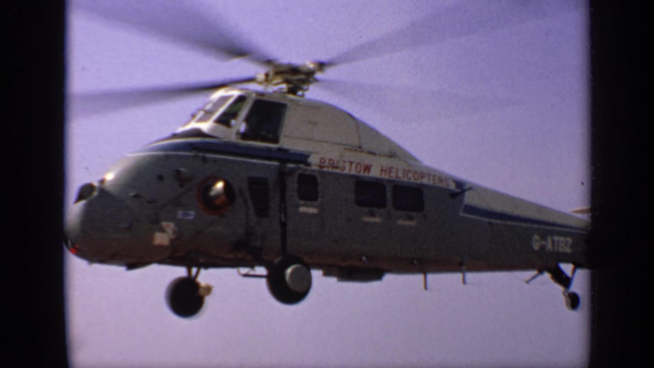 Grey helicopter with Bristol Helicopters lettering flying against a pale sky.
