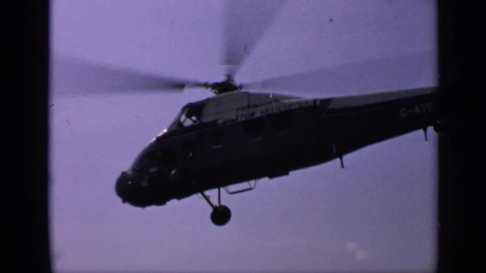 1970 United Kingdom frame showing the helicopter in shadowed side view, with rotor blur and registration marking near the rear.