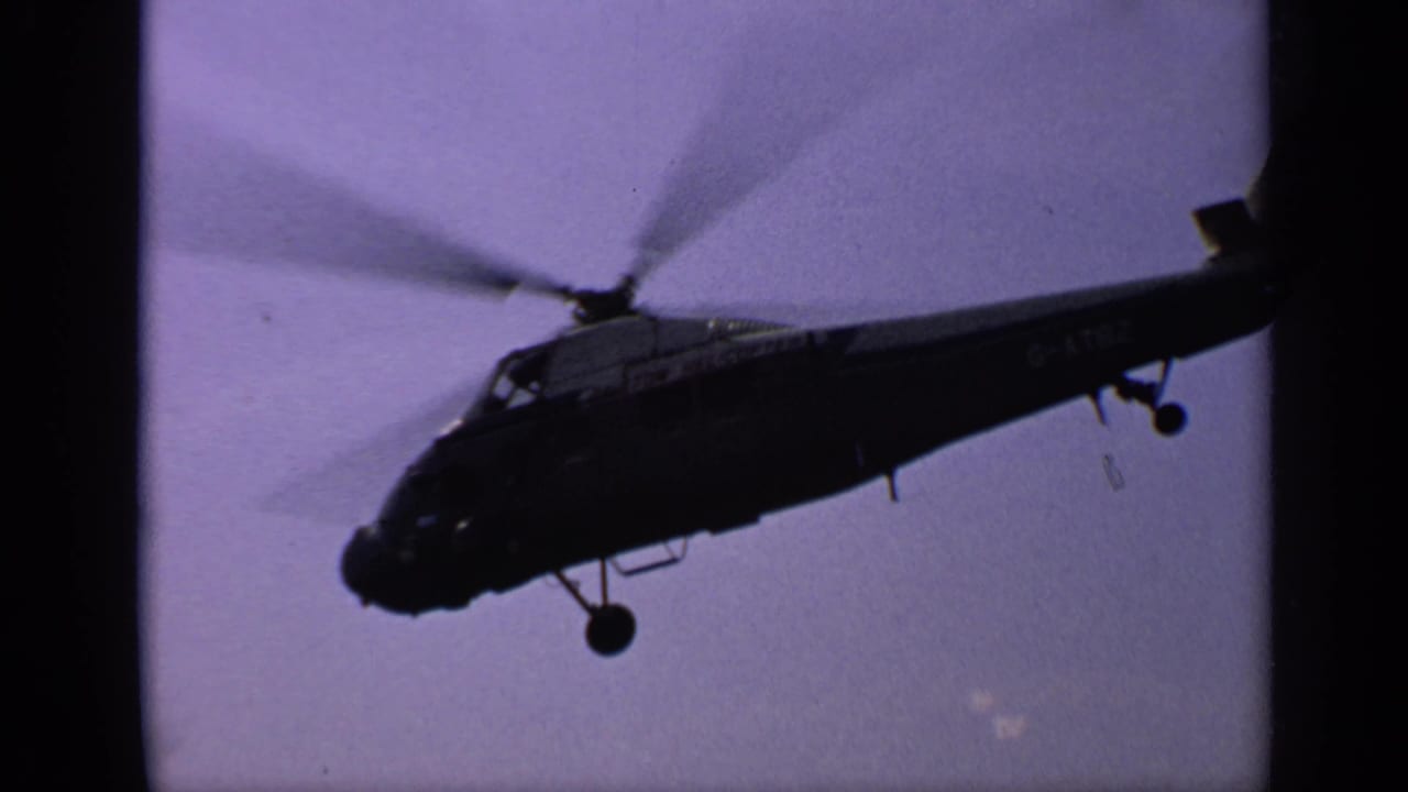 Dark helicopter in flight against a hazy purple sky with blurred rotors and visible side markings.