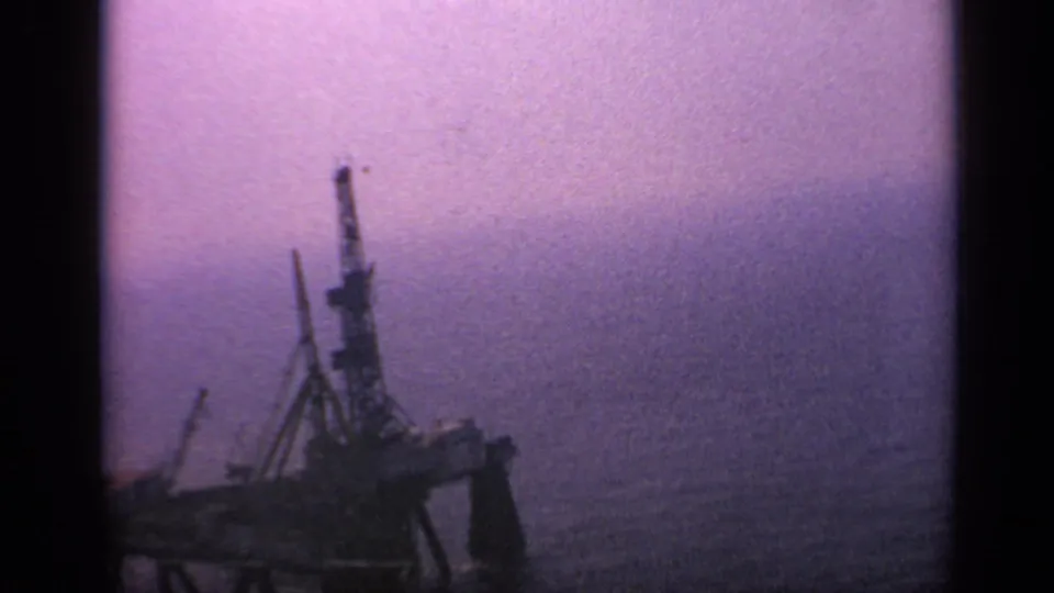 Final 1970 United Kingdom 8mm frame showing the offshore rig or industrial vessel in silhouette beside a broad open-water horizon.