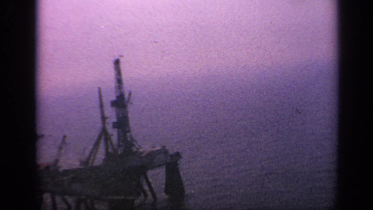 Dark offshore platform silhouette against a hazy purple sea and sky.