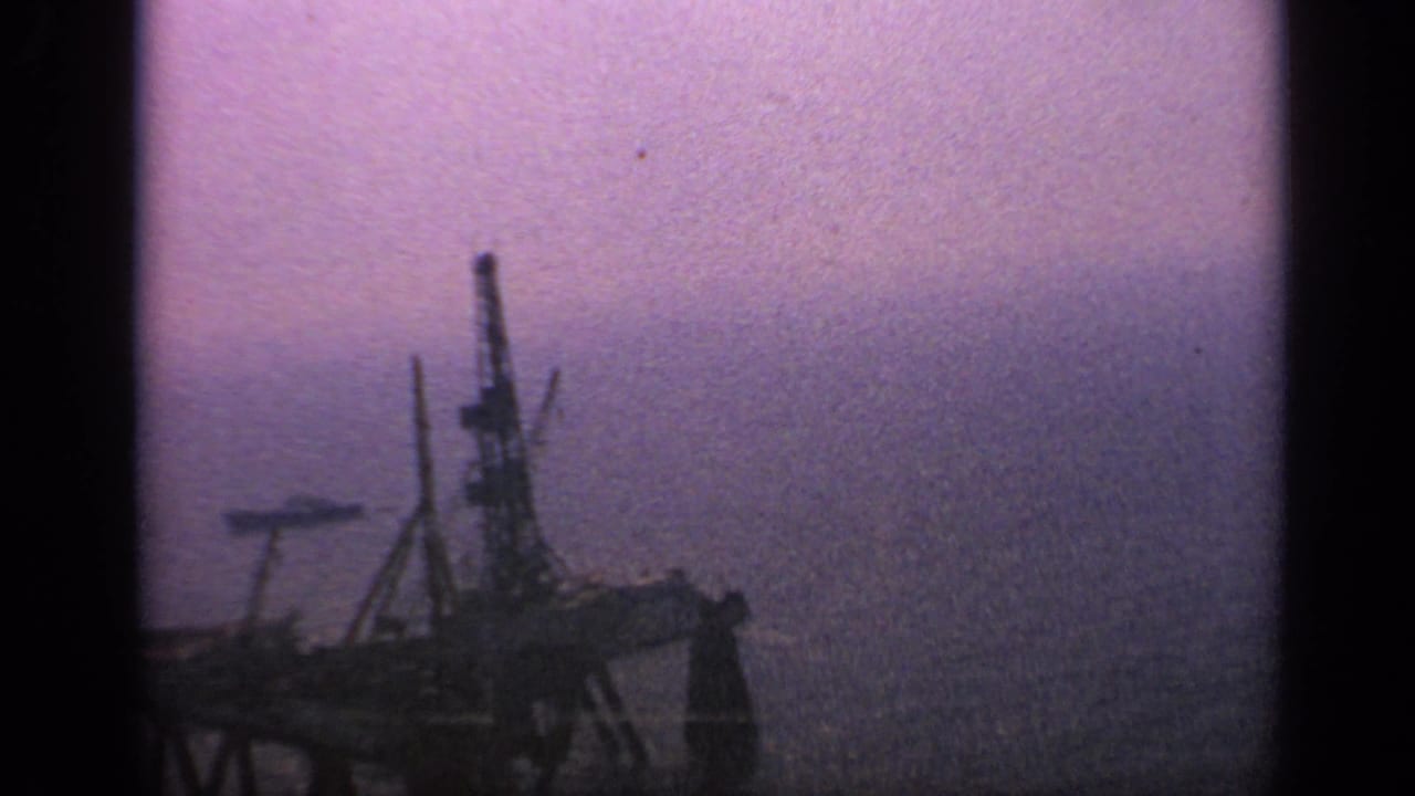 Offshore platform and faint distant ship shape on a hazy ocean horizon.