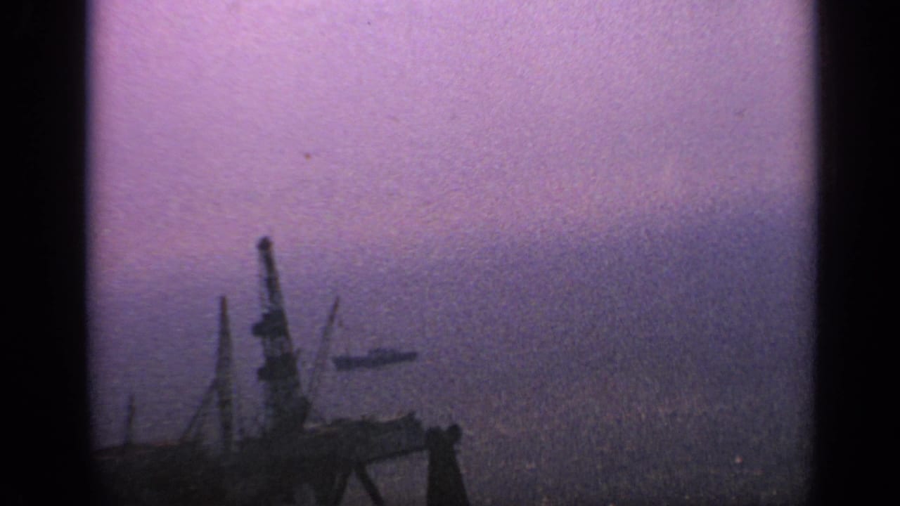 Distant offshore structures and vessels appear through a hazy purple-gray 8mm frame.