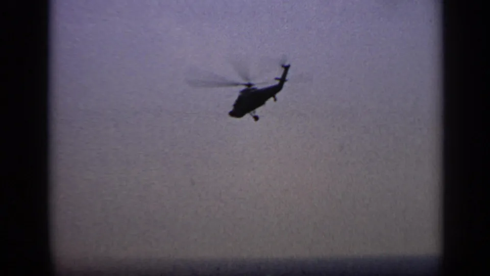 1970 United Kingdom 8mm frame showing the helicopter farther off over water, with haze and grain softening the horizon.