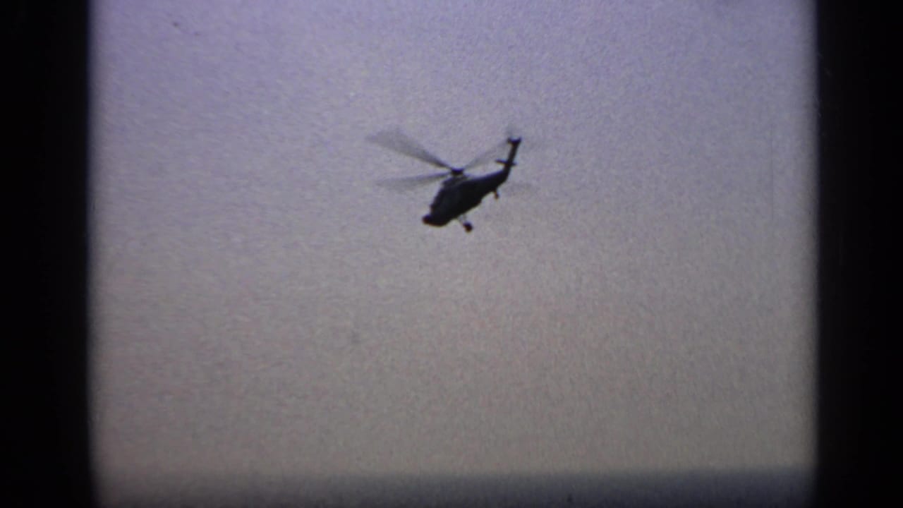Helicopter silhouette flying against a pale sky.