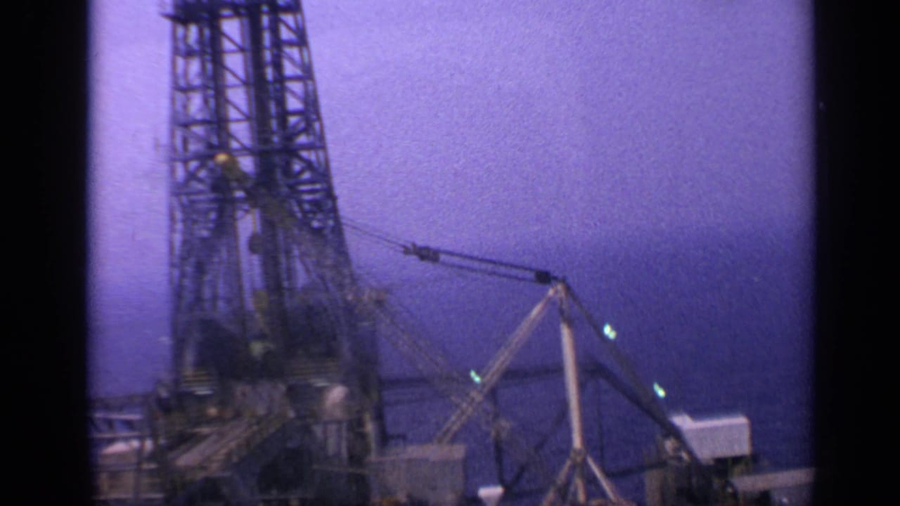 Tall offshore derrick and crane gear silhouetted against purple sky and sea.