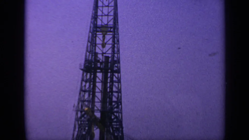 Final 1970 8mm frame holds on the offshore drilling derrick and crane boom, with the industrial structure dark against the dusk sky.