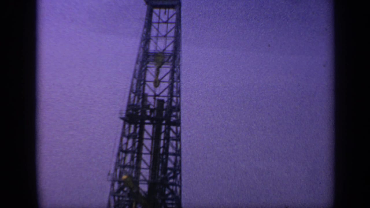 Dark metal rig tower against a purple-tinted sky.