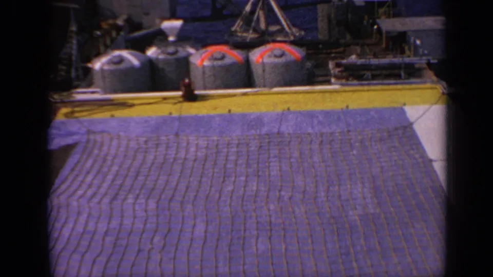 1970 UK 8mm frame showing deck machinery, cylindrical tanks and a large brown net or mat in the foreground.