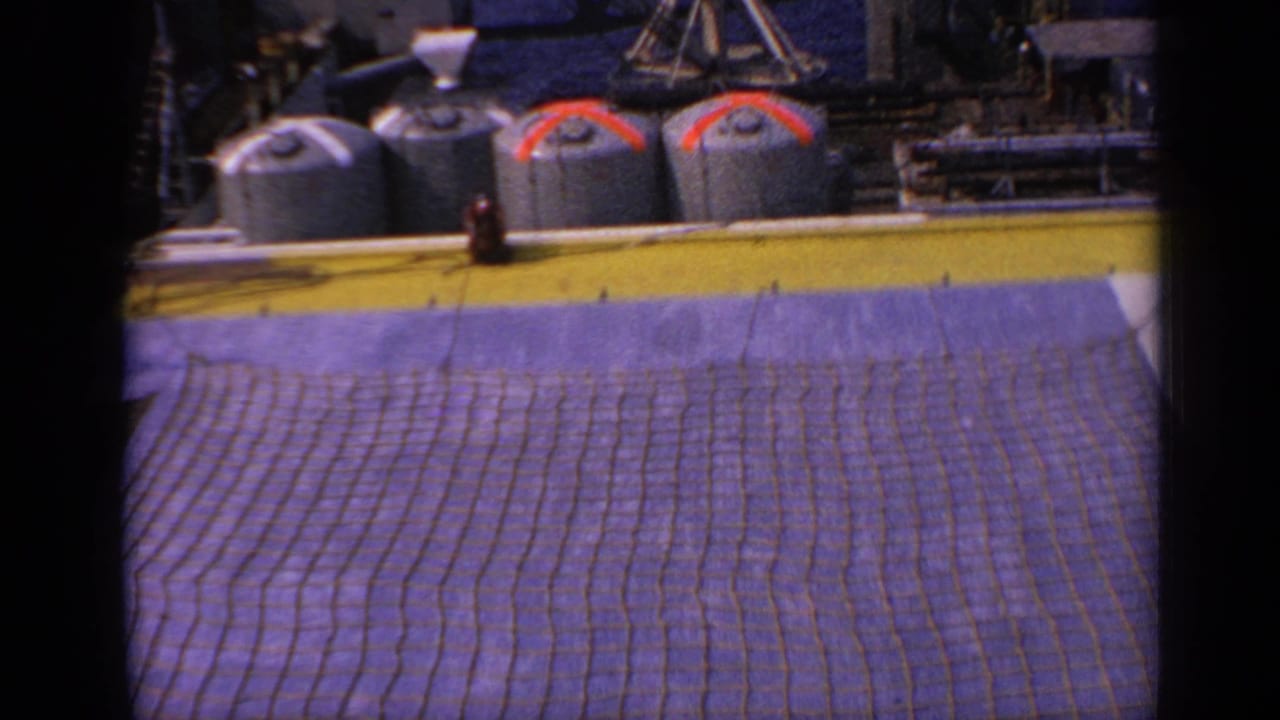 Oil platform deck with cylindrical tanks, yellow rail edge, and purple safety netting.