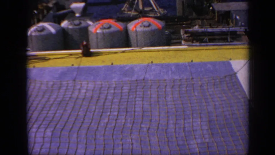 1970 United Kingdom 8mm frame showing platform storage tanks above a broad safety net, with rig equipment in the background.