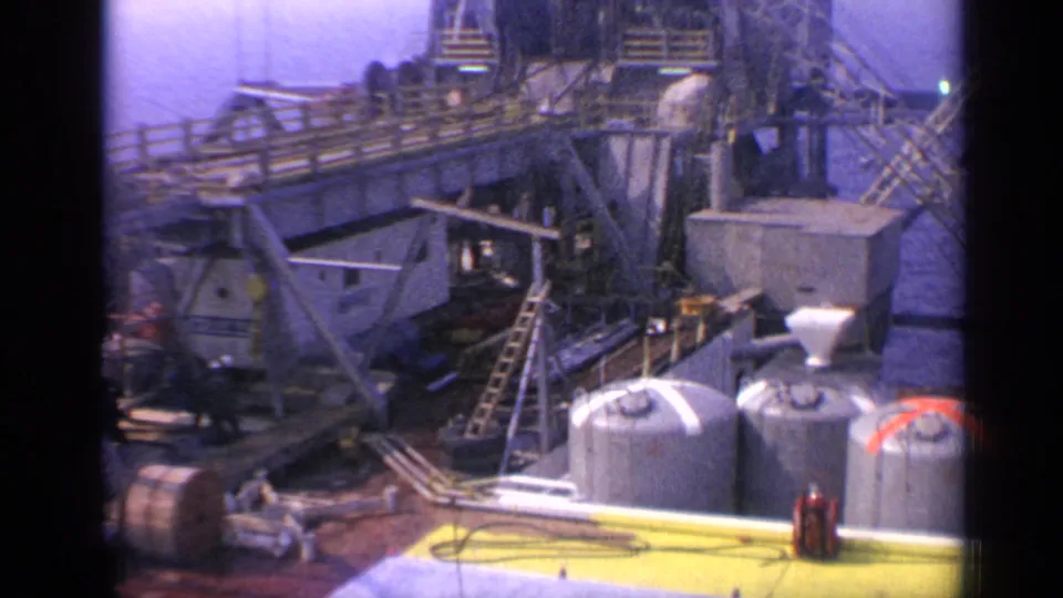 1970 United Kingdom 8mm view across an offshore oil platform deck, showing tanks, ladders, stairs, walkways, and industrial piping.