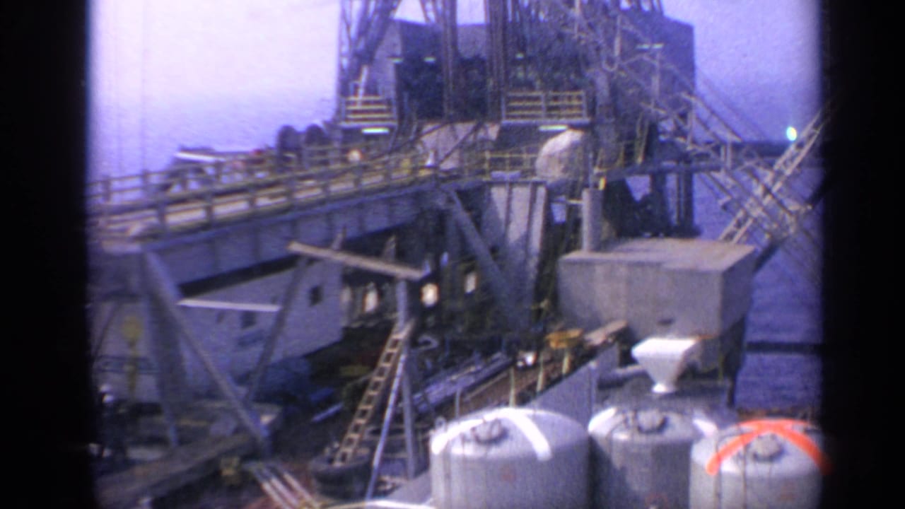 Offshore platform equipment with tanks, walkways, ladders, and rig structures in bright light.