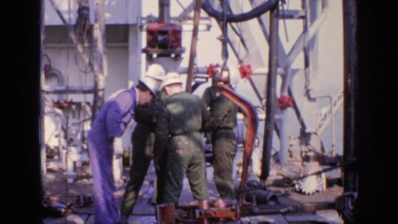 Workers in hard hats gather around machinery, with pipes and cables behind them.
