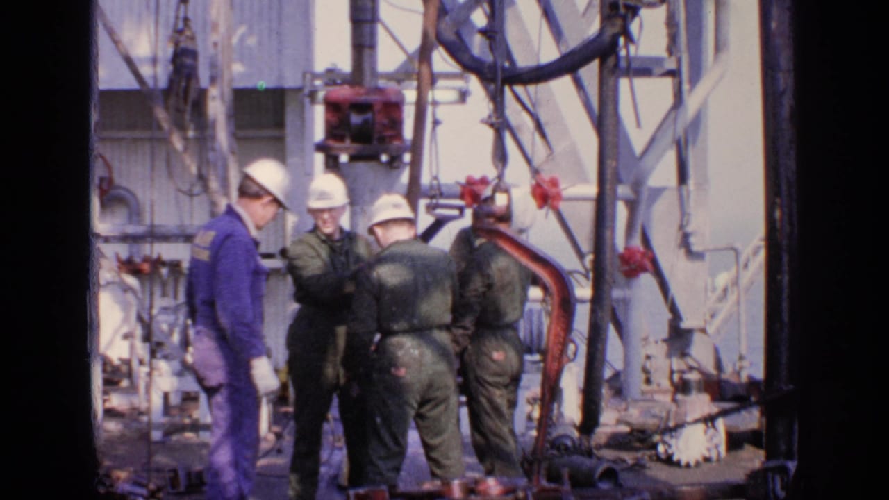 A worker in a purple jumpsuit stands beside men in green coveralls near machinery.