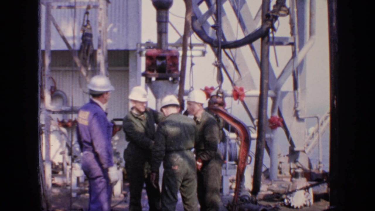 Four hard-hatted workers stand around rig equipment and piping.