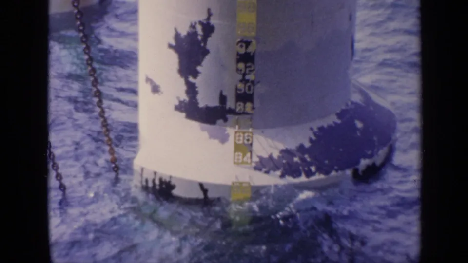 A close view shows a depth gauge or marked equipment beside water, with chains and metal surfaces visible in the frame.