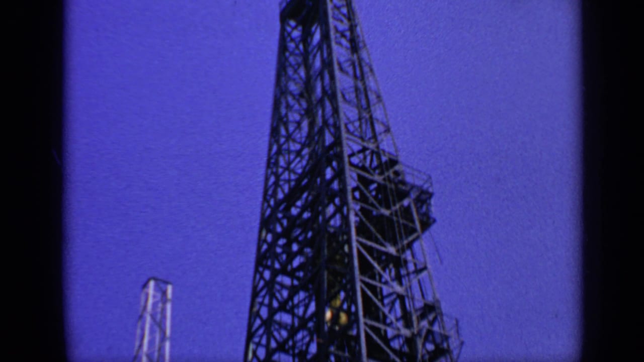 Low-angle view of a tall offshore rig derrick against a deep blue sky.