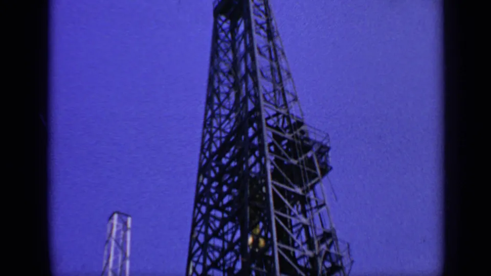 1970 United Kingdom 8mm frame showing a steel offshore oil rig derrick rising against a blue twilight sky.