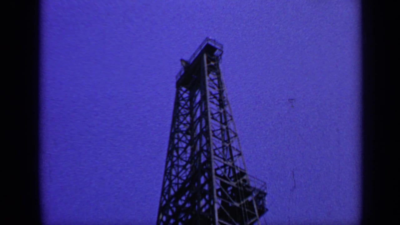 Another low-angle view of the rig derrick with dark film border at center.