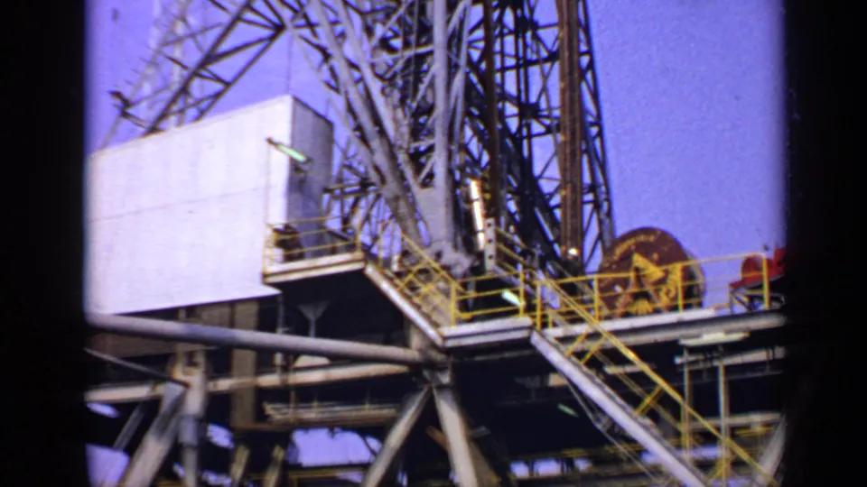 1970 United Kingdom 8mm frame of offshore rig structures, including derrick supports, yellow stair rails, machinery, and platform decking.
